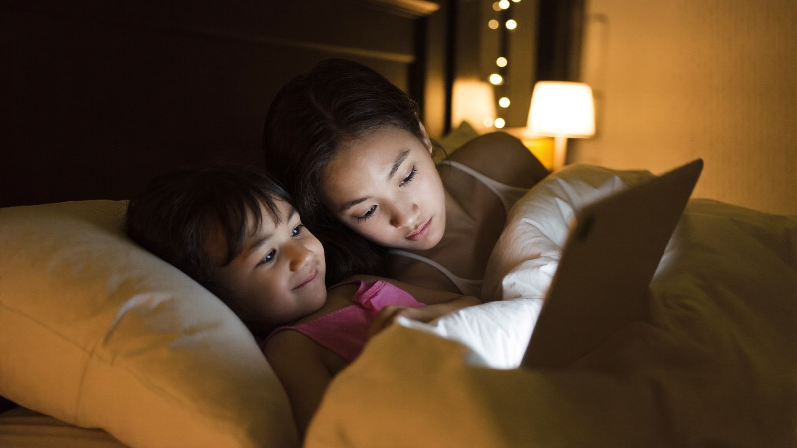 A mom and her daughter snuggled under the covers, calmly watching her bedtime story together